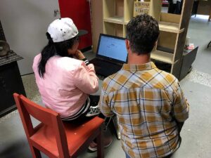 woman sitting on red chair in front of laptop with man in plaid shirt kneeling beside