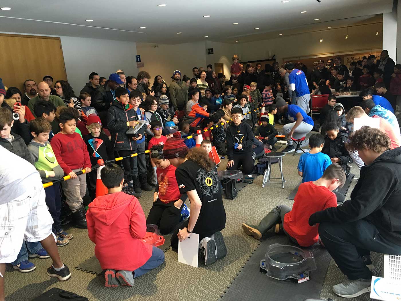 large group of people spectating indoor beyblade tournament