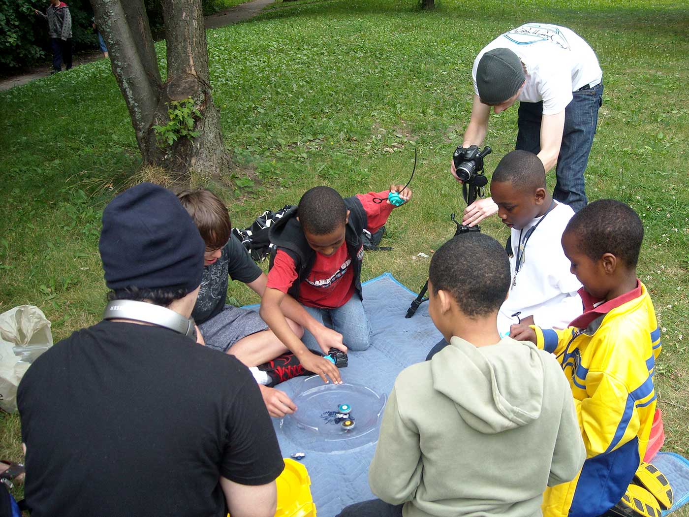 group of people around beyblade stadium on blanket in park