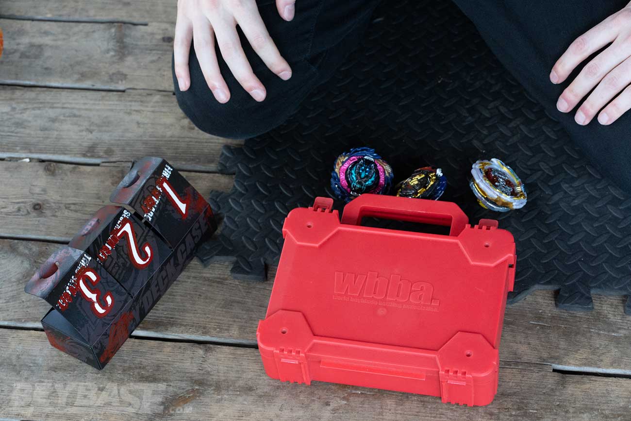 beyblade deck box and wbba deck box with three beyblades sitting on the ground outside it