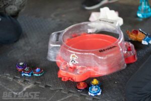 two sets of three beyblades sitting beside red stadium