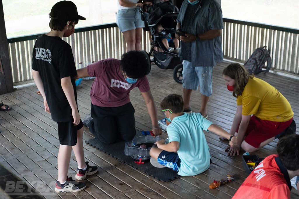 judge and spectator watching two players launch beyblades into stadium