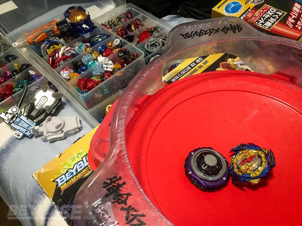 two beyblades sitting inside beyblade burst stadium and opened cases with hundreds of parts