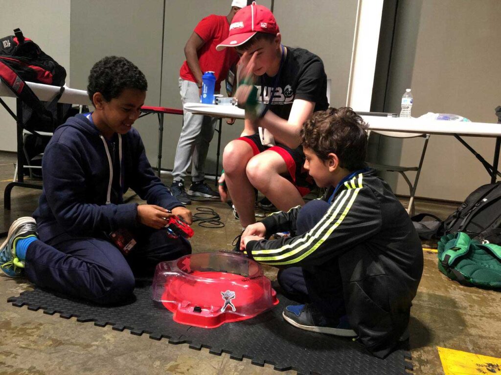 judge performing match countdown while two kids prepare to launch beyblades into stadium