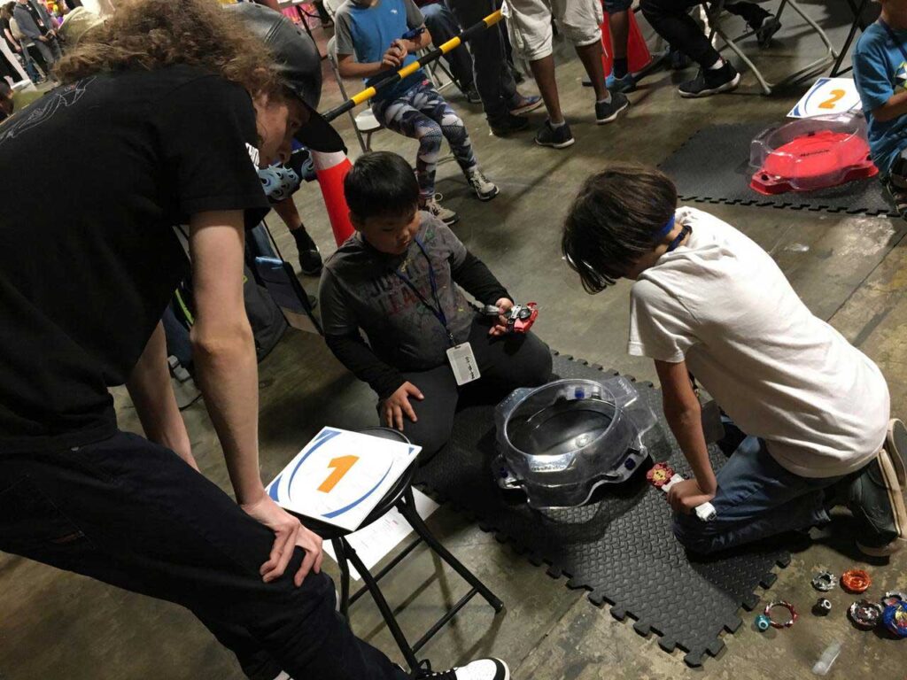 judge standing and looking down on beyblade stadium as two beyblades battle